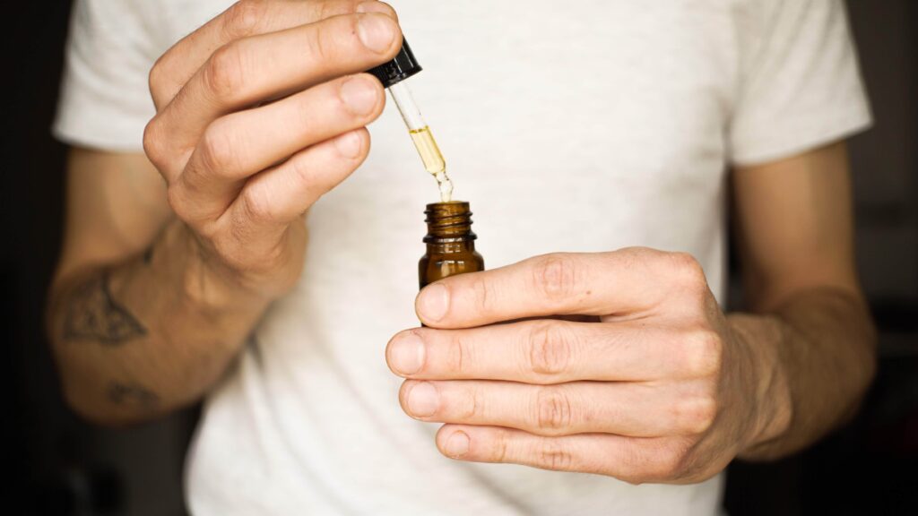 person dropping oil into amber bottle