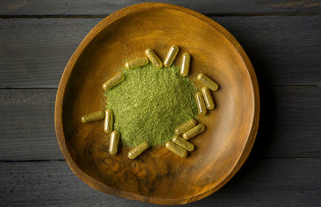 Kratom powder in bowl with capsules