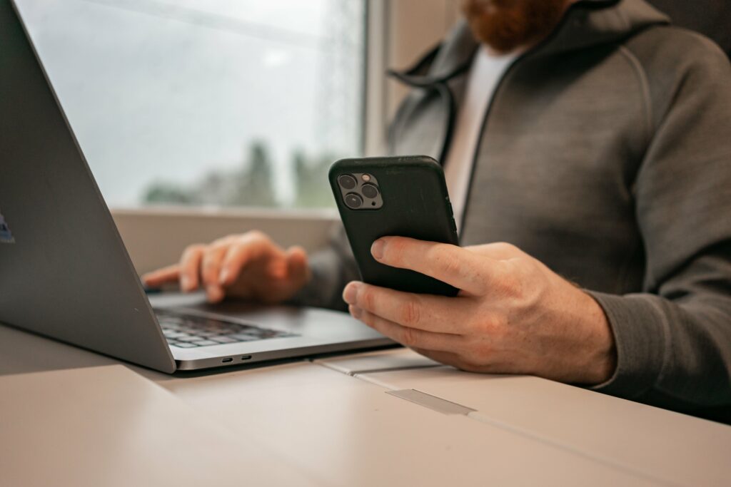 person holding phone in one hand while on laptop